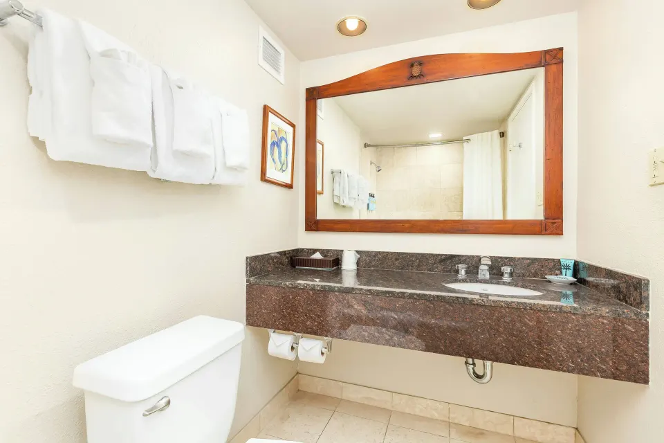 Bathroom vanity with towels and large mirror at Luana Waikiki Hotel & Suites.