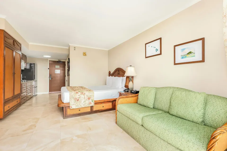 Studio-style room with green sofa and king bed at Luana Waikiki Hotel & Suites.