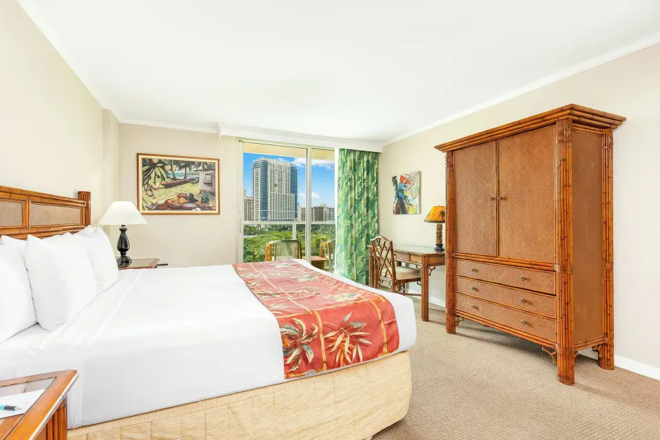 One-bedroom kitchen suite bedroom with king bed and armoire at Luana Waikiki Hotel & Suites.