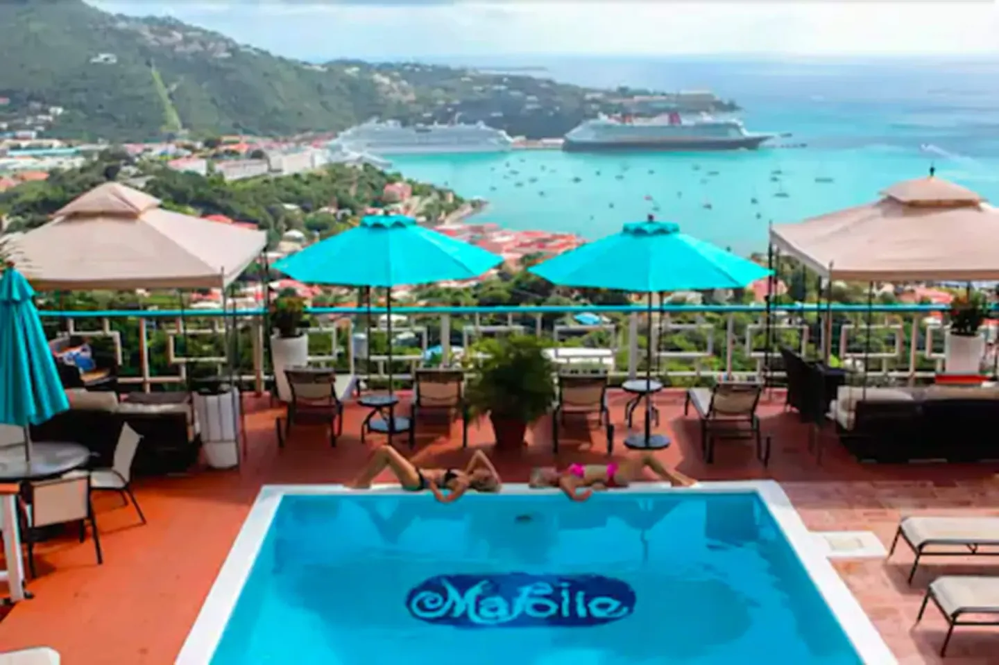 Elevated view of the pool at Mafolie Hotel with sunbathers, umbrellas, harbor, and cruise ships beyond.