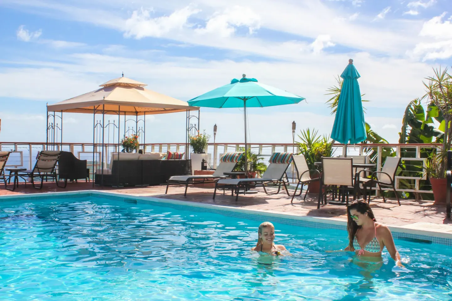 Guests in the pool at Mafolie Hotel with lounge chairs, umbrellas, and ocean beyond the deck.