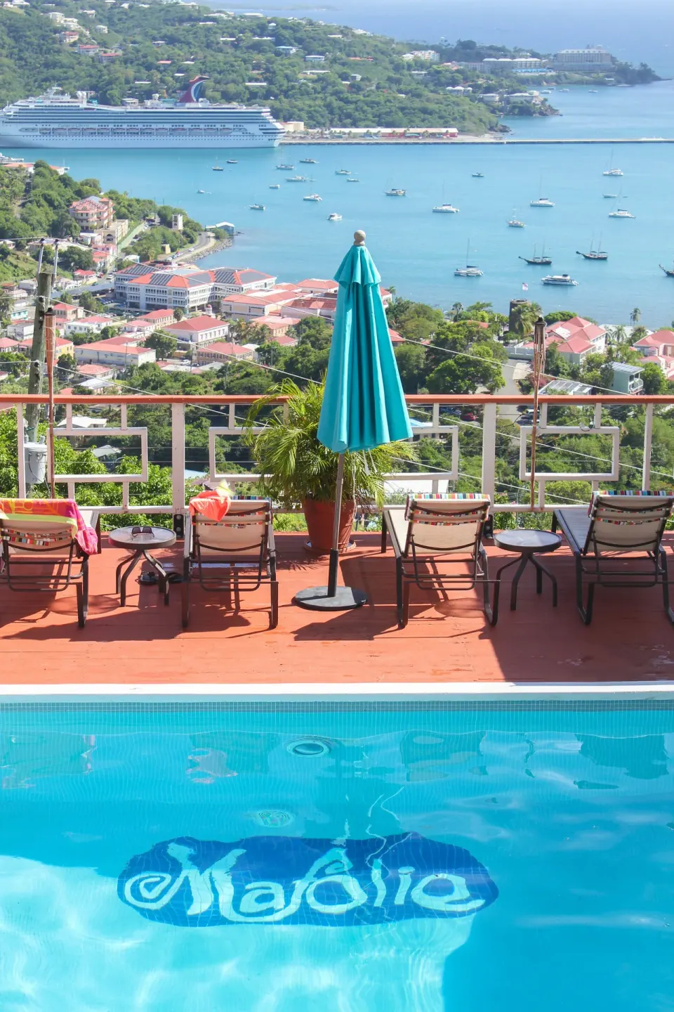 Pool deck at Mafolie Hotel overlooking the harbor with lounge chairs, umbrellas, and boats below.
