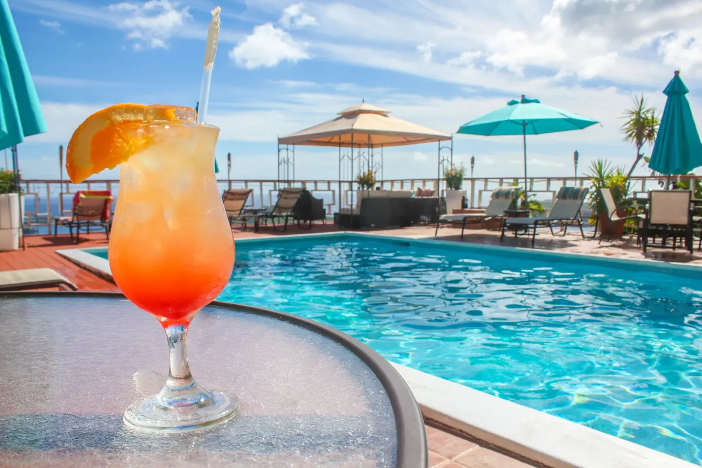 Tropical drink beside the pool at Mafolie Hotel with umbrellas and lounge seating in the background.