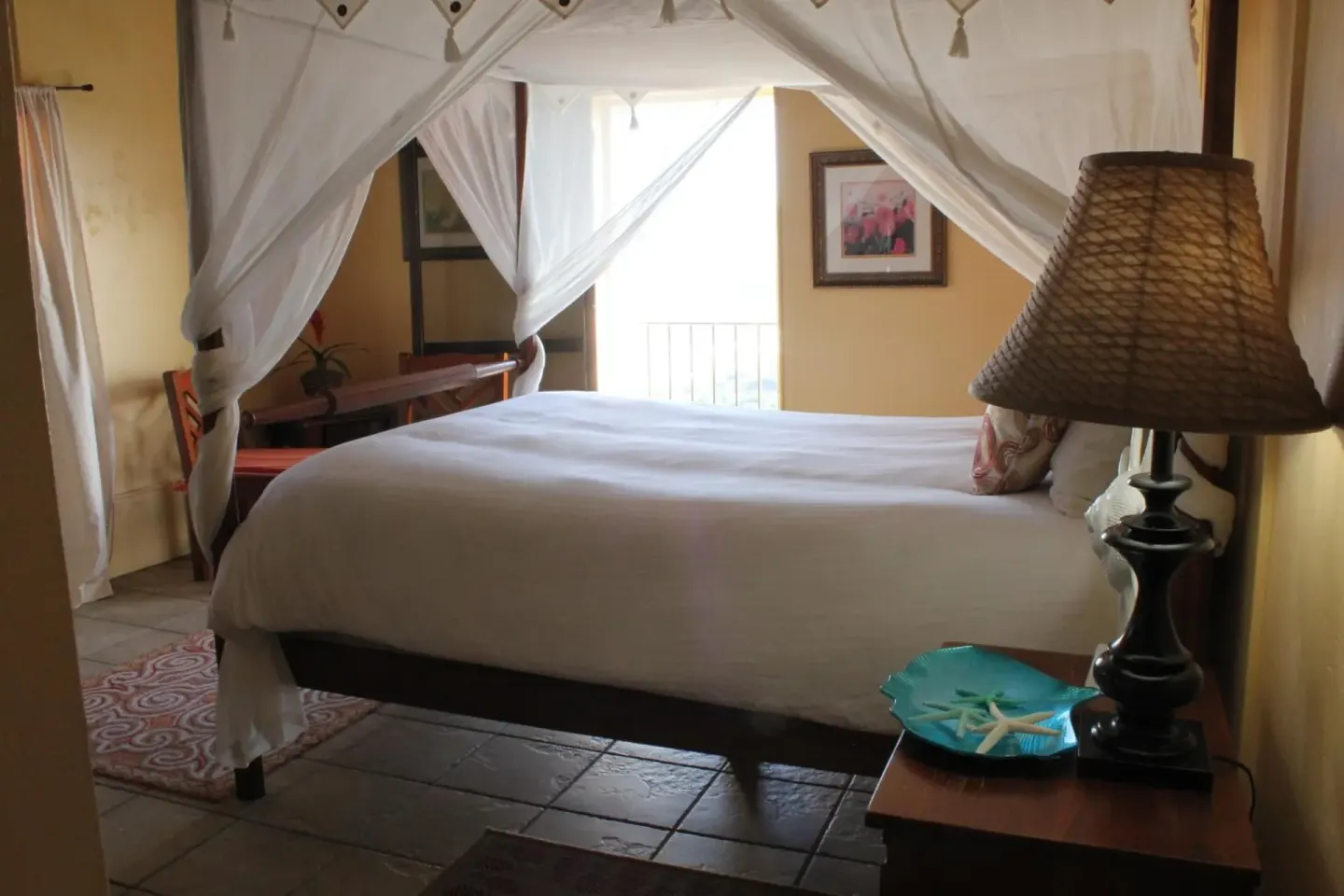 Deluxe Room canopy bed with bedside lamp, tile floor, and balcony doors at Mafolie Hotel.
