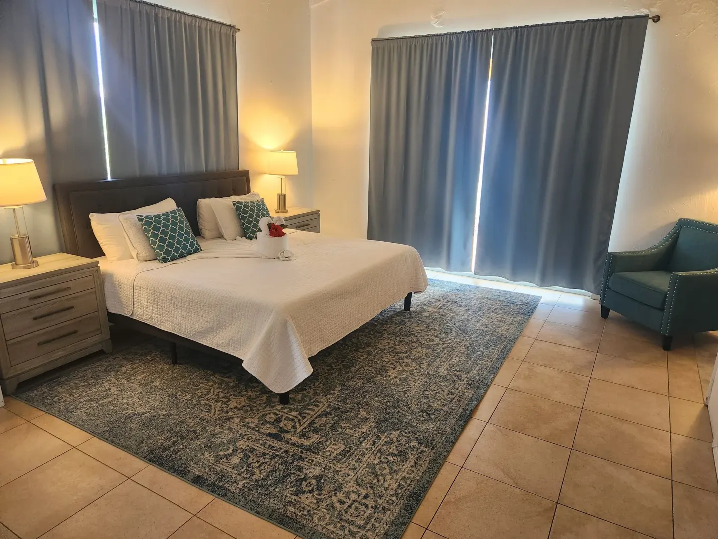 Panoramic Villa bedroom with bed, curtains, rug, and teal chair at Mafolie Hotel.