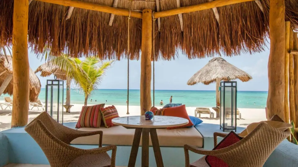 Shaded palapa seating with chairs facing sandy beach and turquoise sea at Mahekal Beach Front Resort & Spa