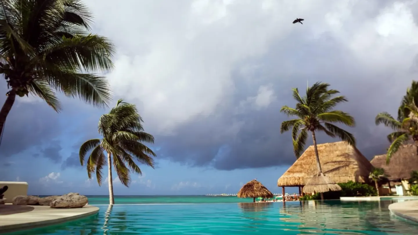 Beachfront pool, palms, thatched roofs, and storm clouds at Mahekal Beach Front Resort & Spa.