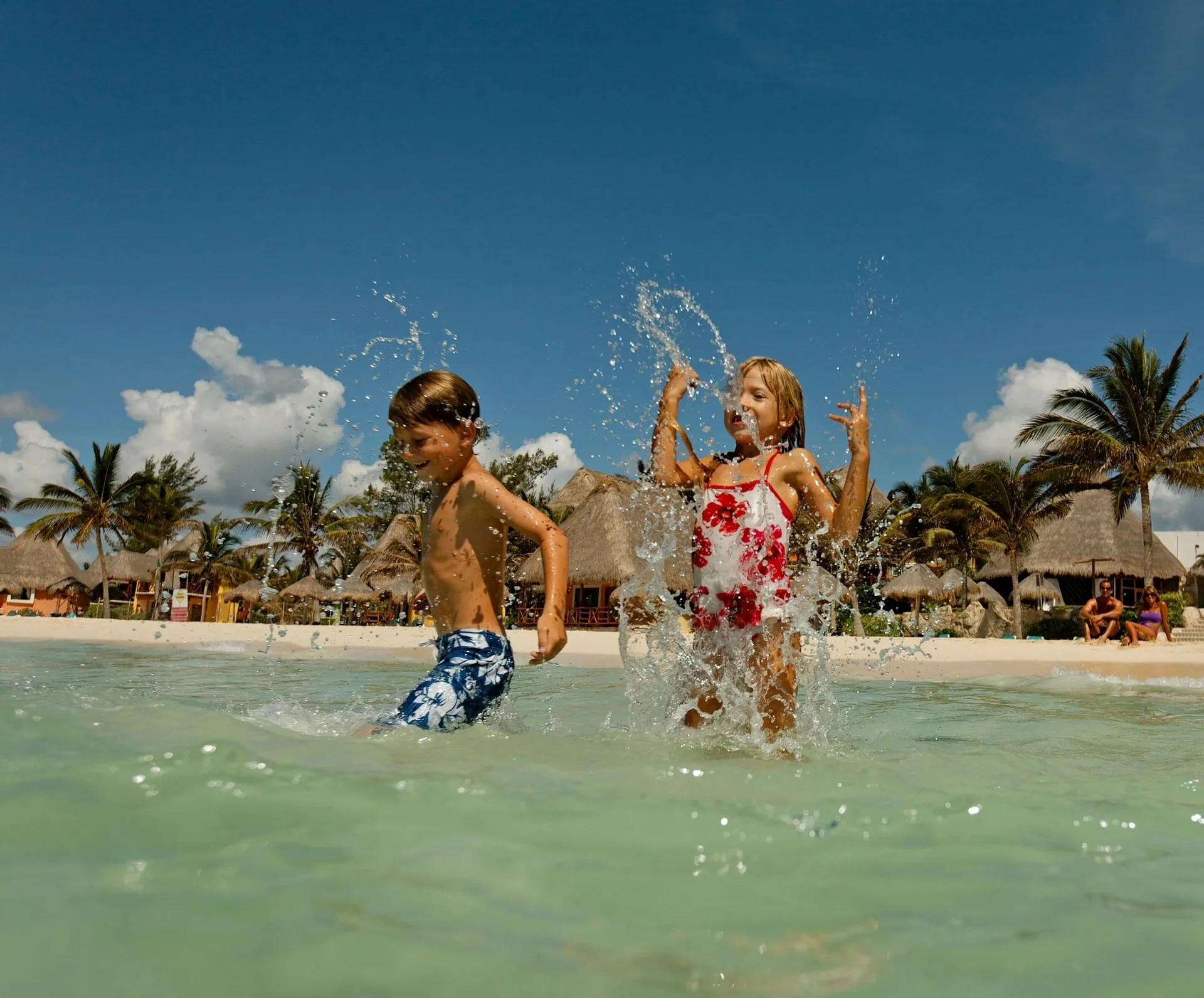 Children splashing in shallow beach water at Mahekal Beach Front Resort & Spa.