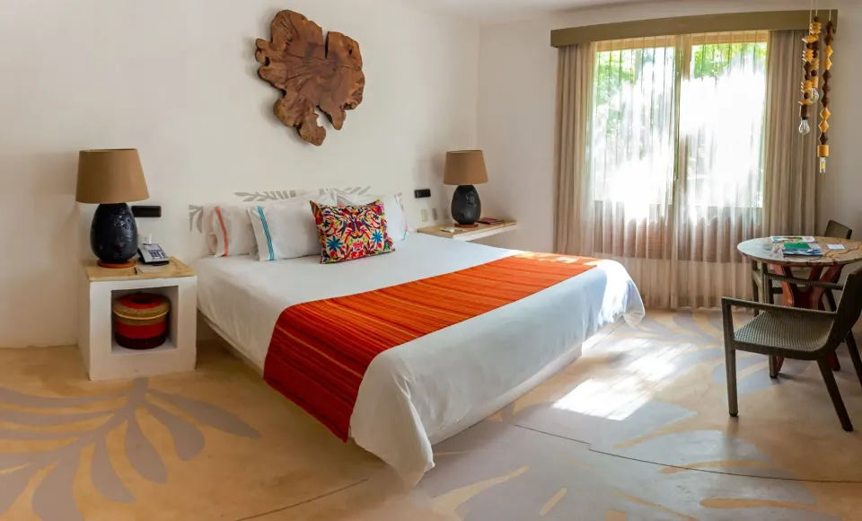Sunlit guest room with king bed, bedside lamps and a small table at Mahekal Beach Front Resort & Spa