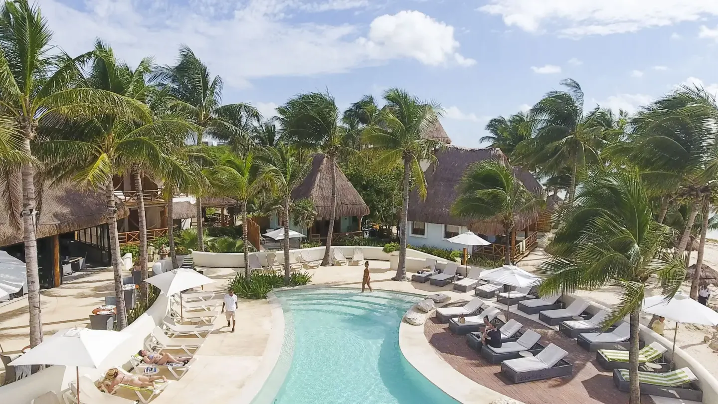 Resort pool surrounded by palms and thatched buildings at Mahekal Beach Front Resort & Spa.