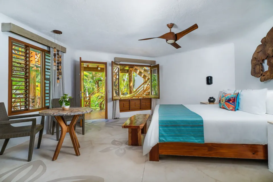 Spacious guest room with king bed, table and open windows to tropical foliage at Mahekal Beach Front Resort & Spa