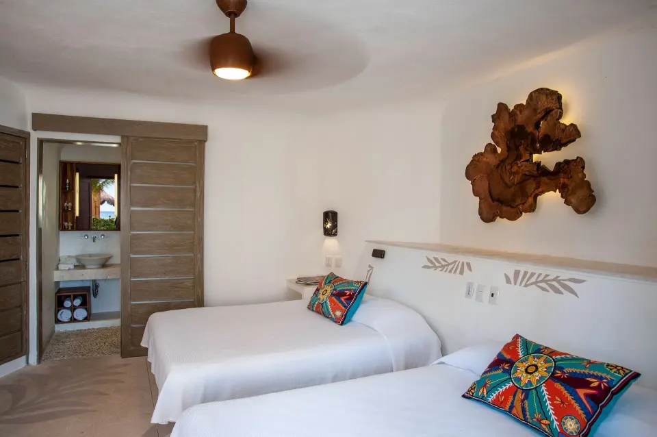 Bright guest room with twin beds and colorful pillows at Mahekal Beach Front Resort & Spa
