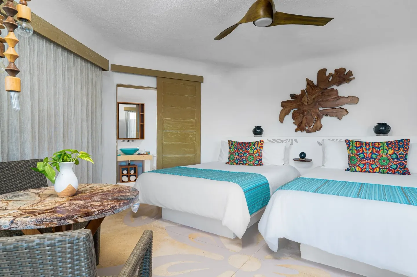 Guest room with two beds, dining table, and colorful pillows at Mahekal Beach Front Resort & Spa.