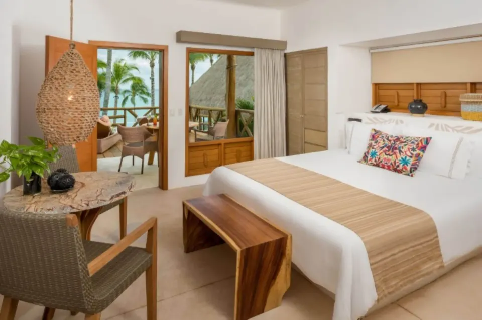 Bright guest room with king bed and balcony overlooking palms at Mahekal Beach Front Resort & Spa