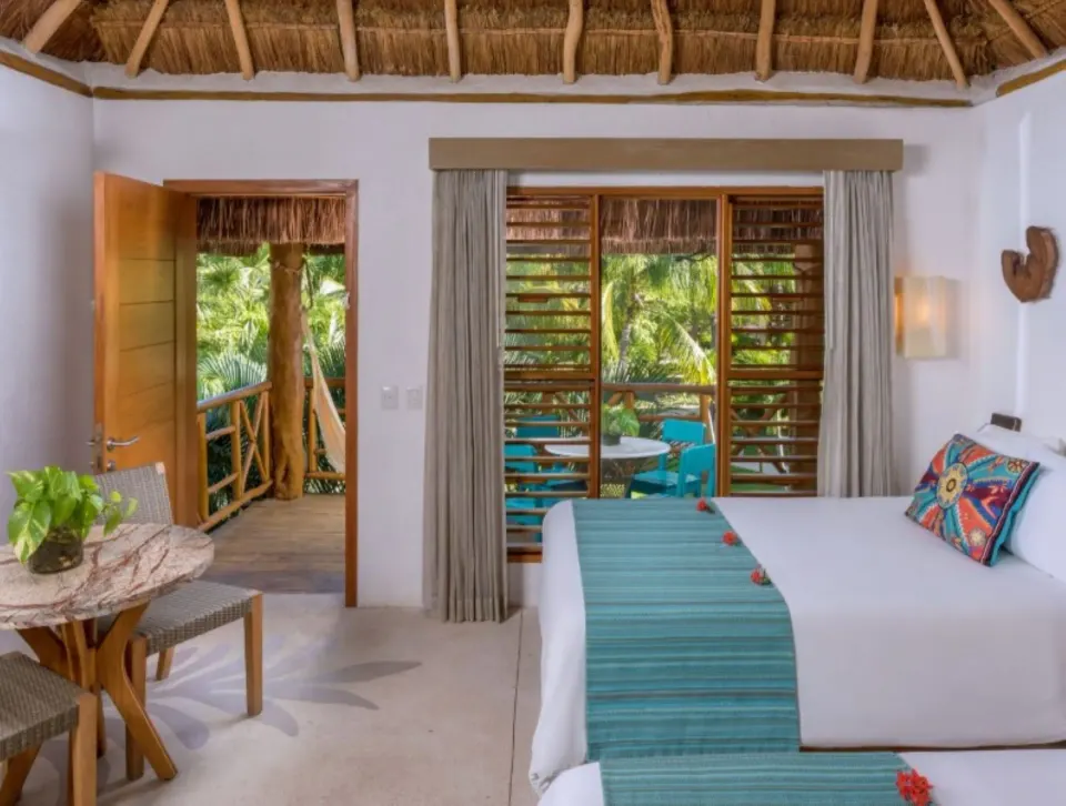 Guest room twin beds with balcony doors open to foliage at Mahekal Beach Front Resort & Spa