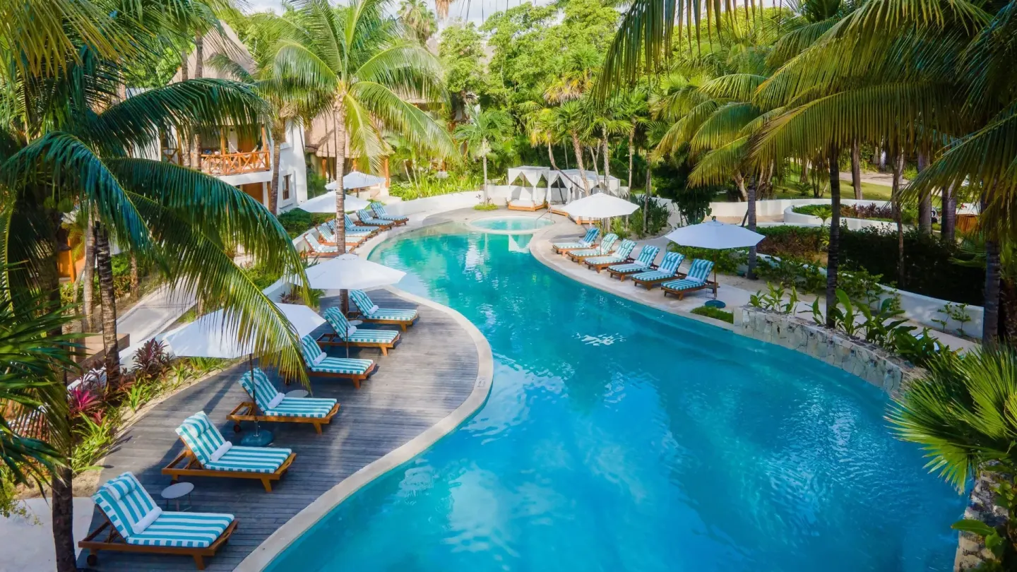 Curving resort pool with striped loungers and palm trees at Mahekal Beach Front Resort & Spa.