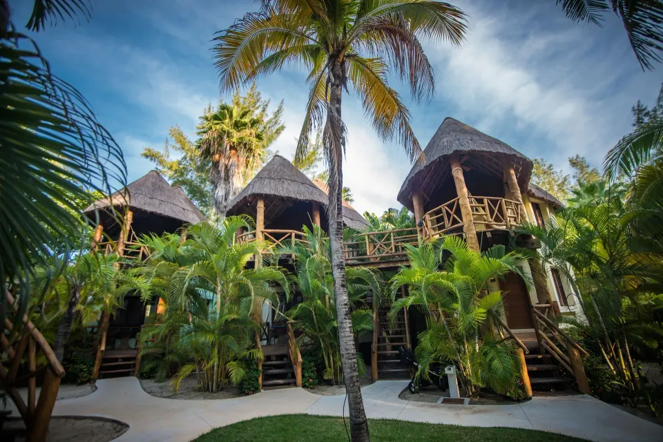 Raised thatched bungalows connected by walkways among palms at Mahekal Beach Front Resort & Spa