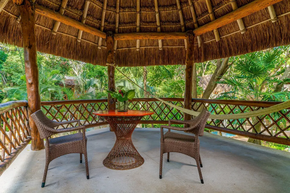 Thatched gazebo with wicker table and chairs amid palms at Mahekal Beach Front Resort & Spa