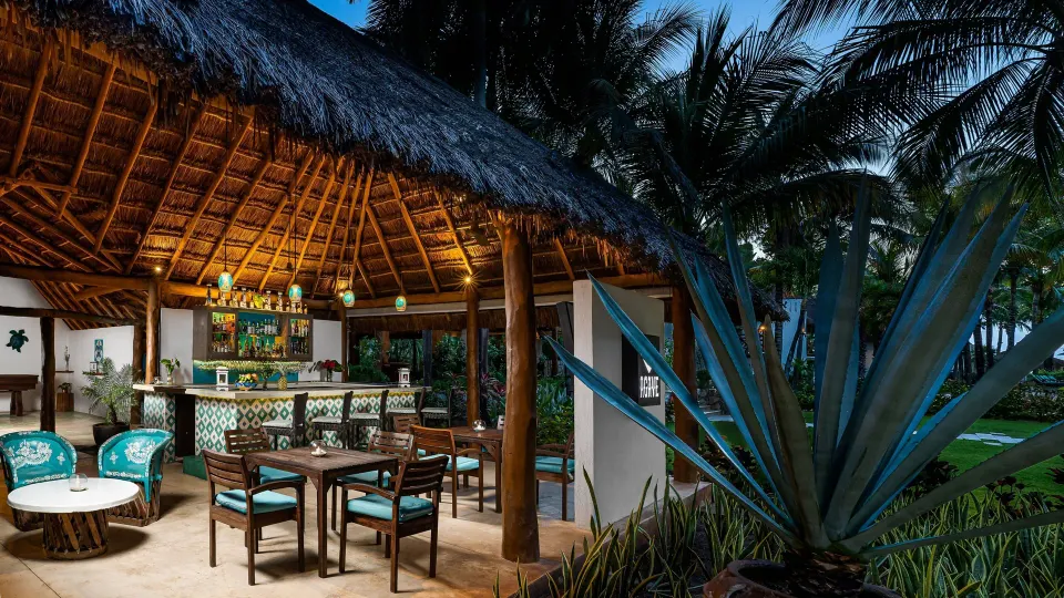 Thatched bar interior with seating and agave plant at Mahekal Beach Front Resort & Spa