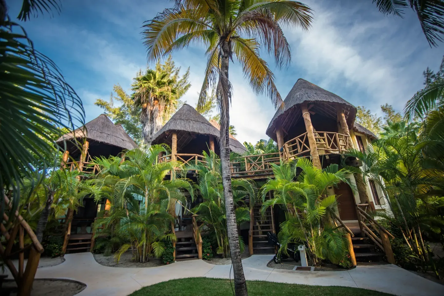 Garden View room buildings with thatched balconies among palms at Mahekal Beach Front Resort & Spa.
