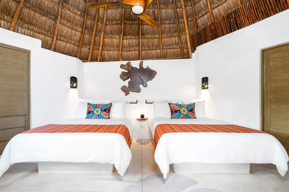 Head-on view of two beds under a palapa roof in a Garden View room at Mahekal Beach Front Resort & Spa