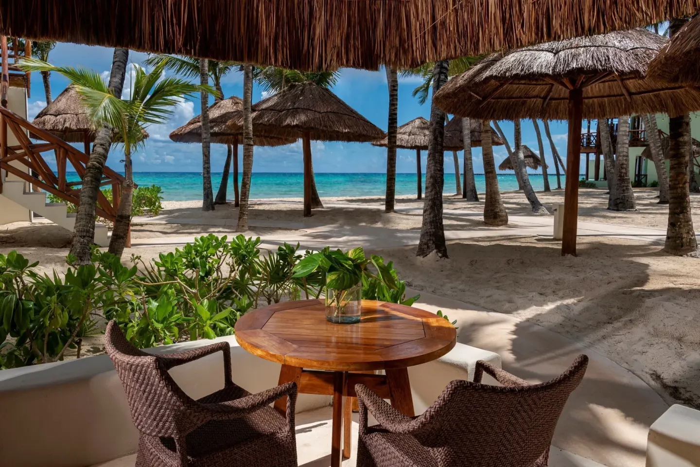 Ocean View room patio with table, chairs, palms, and beach at Mahekal Beach Front Resort & Spa.