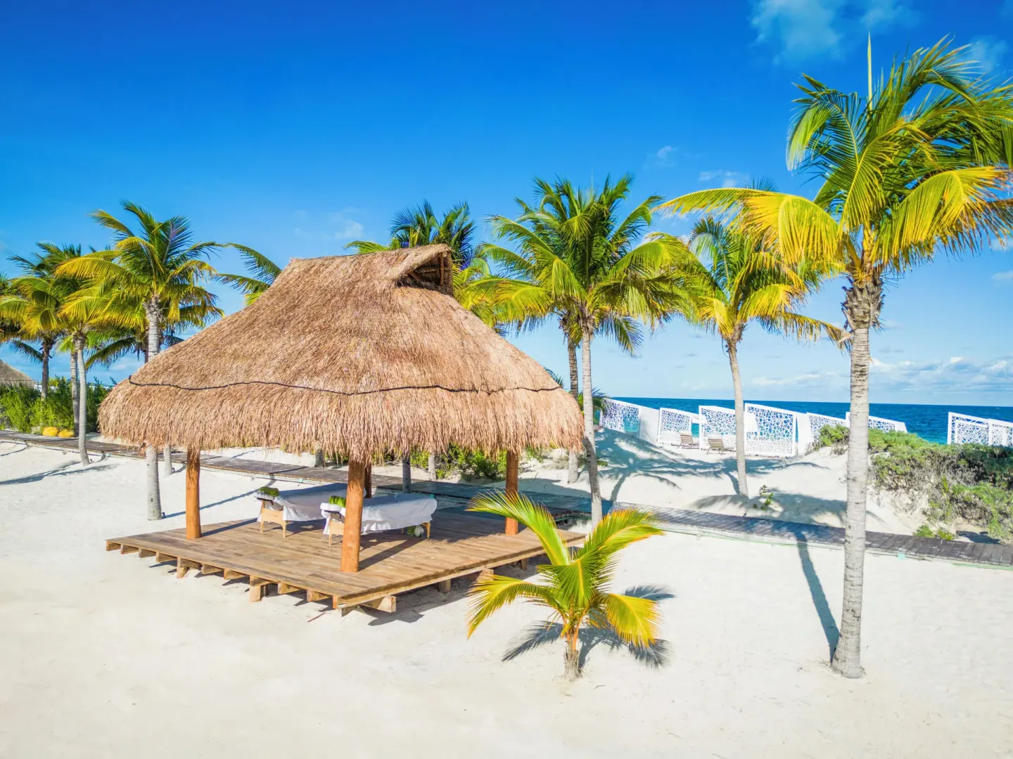 Beach palapa with massage tables and palm trees at Majestic Elegance Costa Mujeres.