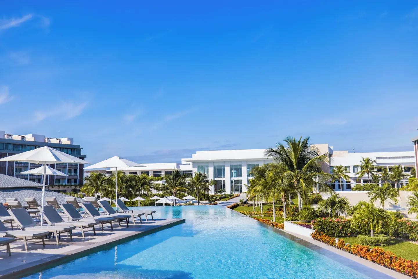Long pool with loungers, umbrellas, palms, and resort buildings at Majestic Elegance Costa Mujeres.