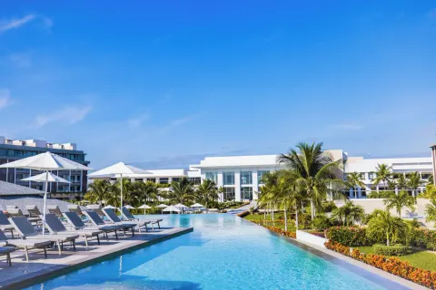 Long pool with loungers, umbrellas, palms, and resort buildings at Majestic Elegance Costa Mujeres.