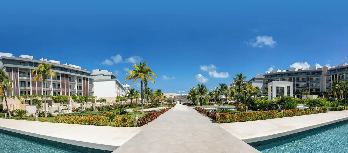 Palm-lined resort walkway between pools and buildings at Majestic Elegance Costa Mujeres.