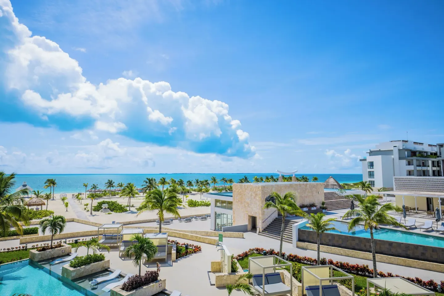 Resort pools, palms, and beach facing the sea at Majestic Elegance Costa Mujeres.