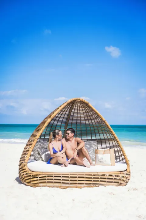Couple seated on a wicker beach daybed at Majestic Elegance Costa Mujeres.
