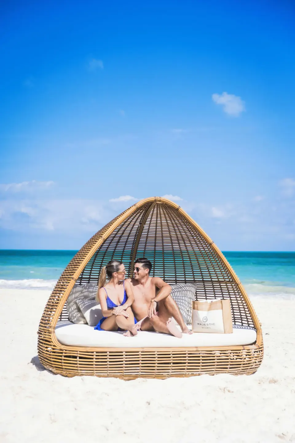Couple seated on a wicker beach daybed at Majestic Elegance Costa Mujeres.