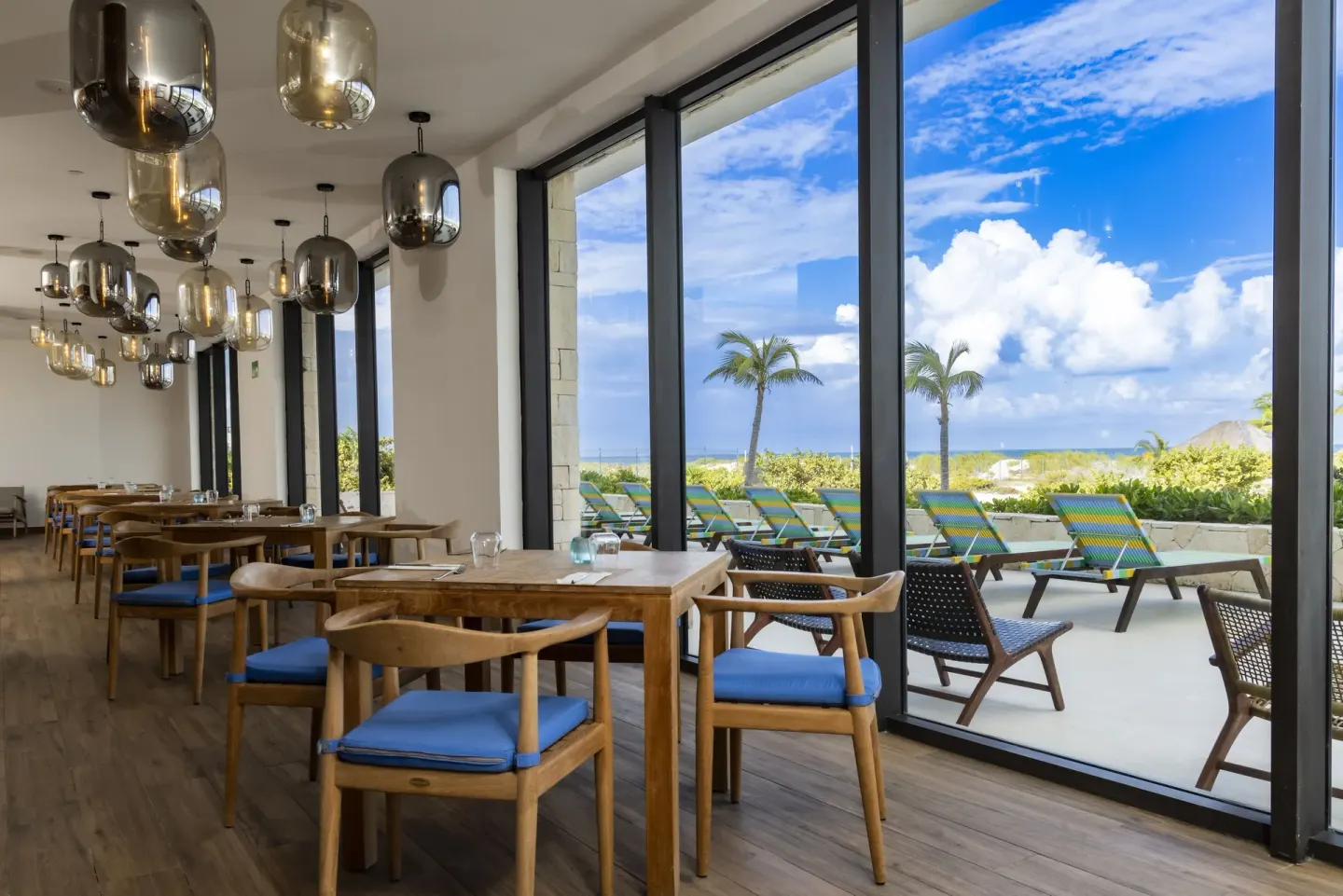 Ocean-facing dining room with blue-cushioned chairs at Majestic Elegance Costa Mujeres.