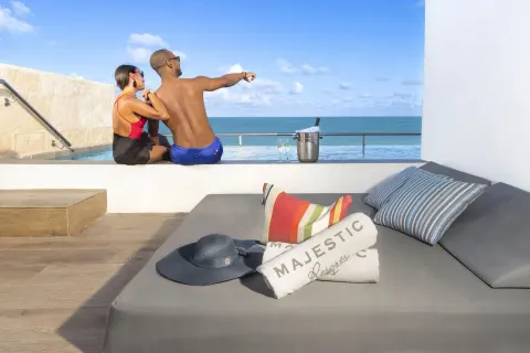Terrace daybed and oceanfront plunge pool at Majestic Elegance Costa Mujeres with guests by the water.
