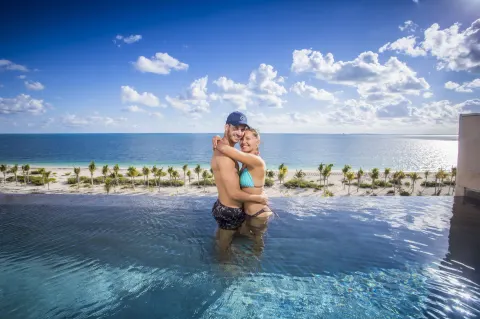 Couple in an oceanfront plunge pool at Majestic Elegance Costa Mujeres overlooking the beach.