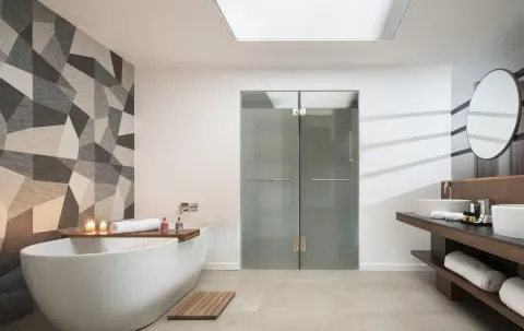 Junior Suite bathroom at Majestic Elegance Costa Mujeres with tub, frosted shower doors, and double vanity.