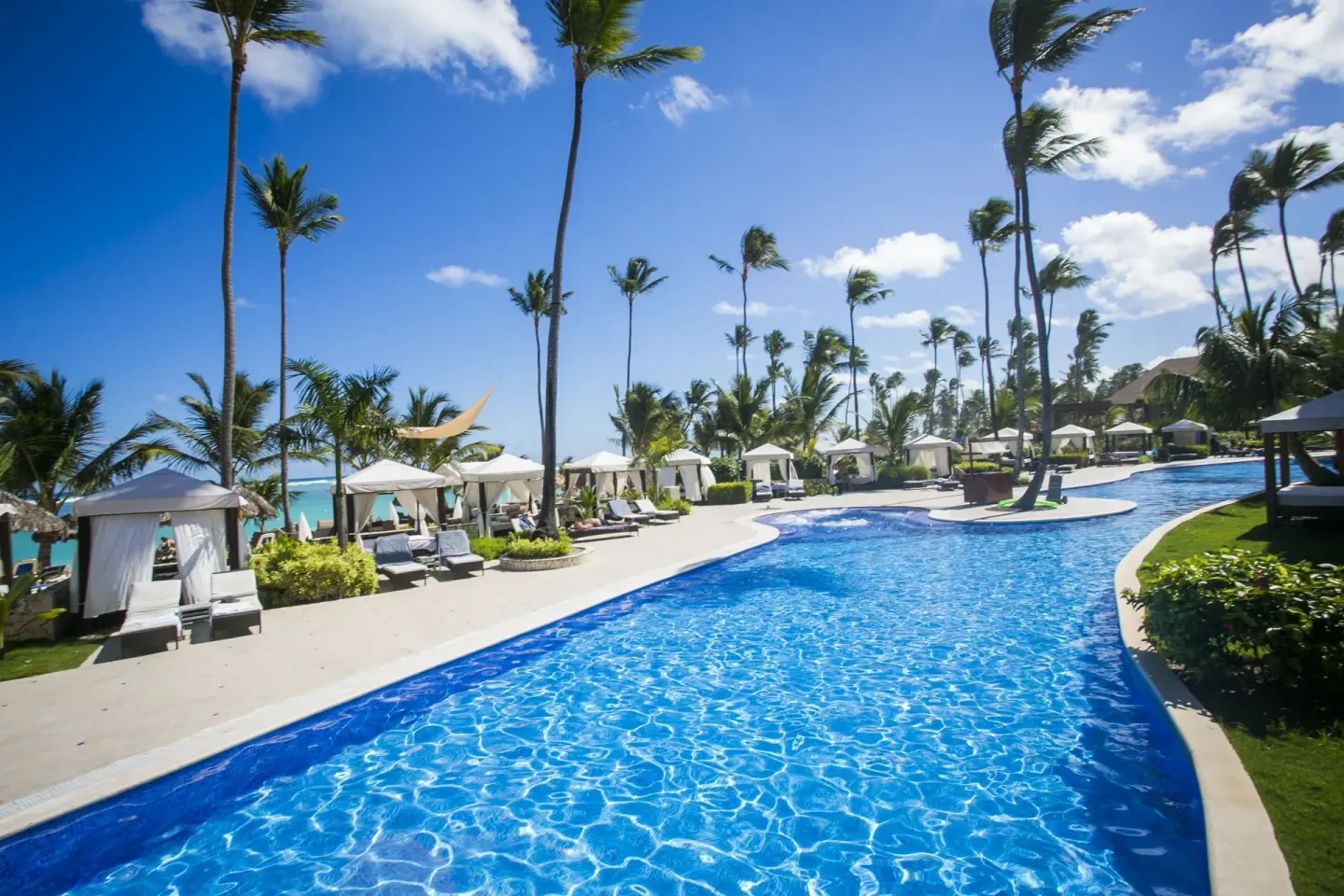Beachside pool with cabanas and tall palms at Majestic Elegance Punta Cana.