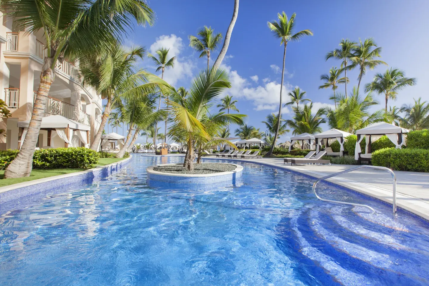 Curving pool with palm island and cabanas at Majestic Elegance Punta Cana.