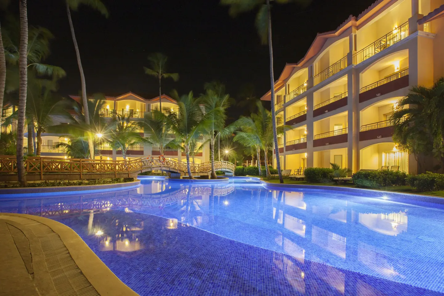 Illuminated pool, palms, and guest buildings at night at Majestic Elegance Punta Cana.