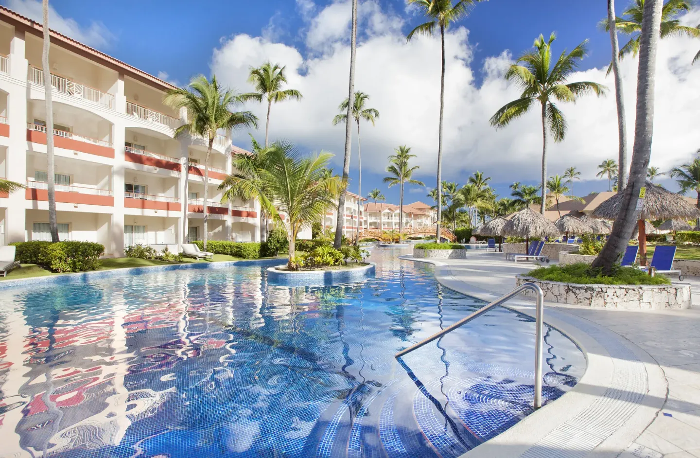 Swim-up style pool beside guest buildings and palapas at Majestic Elegance Punta Cana.