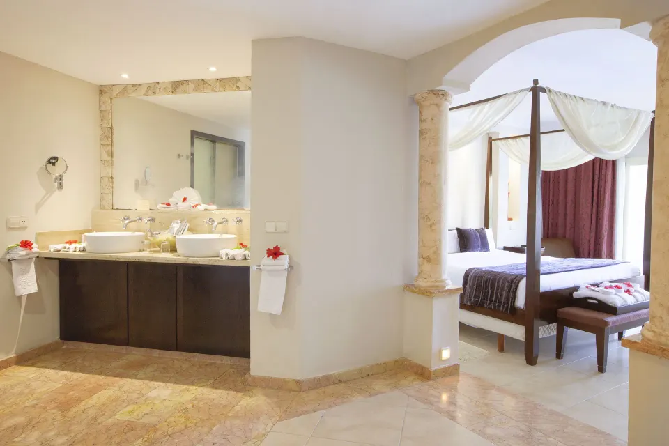 One Bedroom Suite bathroom vanity and king bed at Majestic Elegance Punta Cana with open archway.