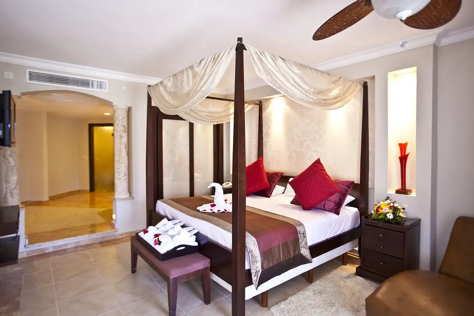 One Bedroom Suite king canopy bed at Majestic Elegance Punta Cana with towel decor and sitting area.