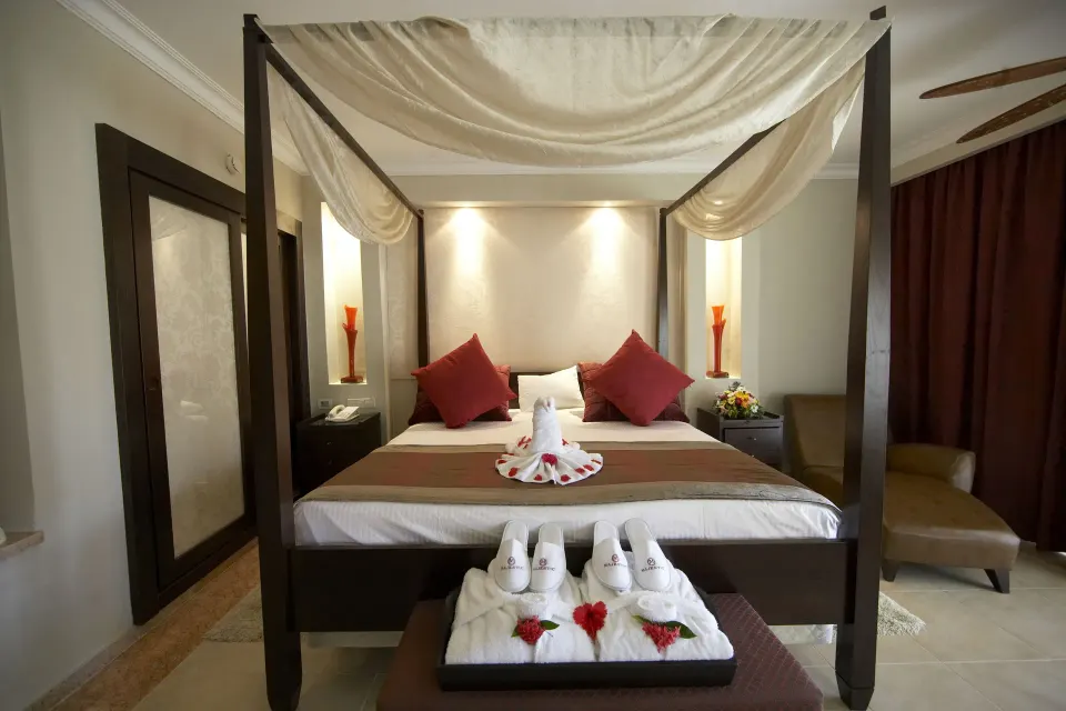 One Bedroom Suite king canopy bed at Majestic Elegance Punta Cana with robes and red accents.