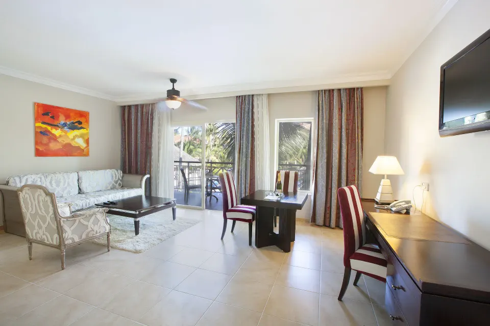 One Bedroom Suite living area at Majestic Elegance Punta Cana with sofa, dining table, desk, and balcony.