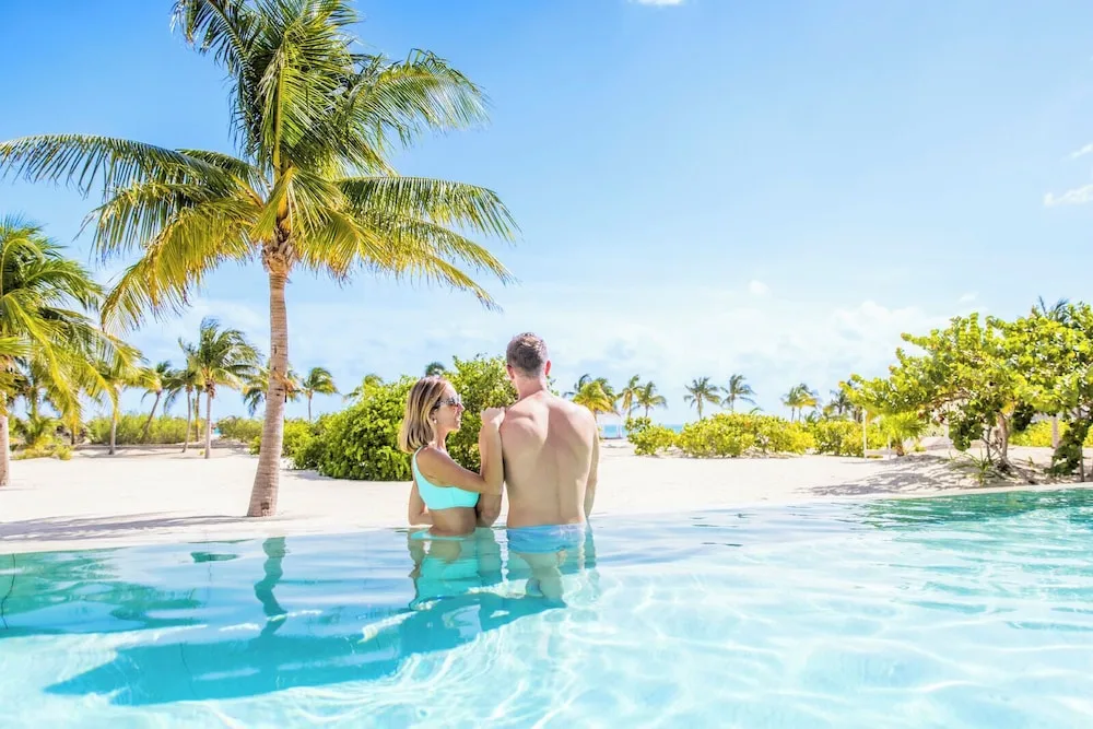 Guests standing in a pool facing palms and the beach at Majestic Mirage Costa Mujeres.