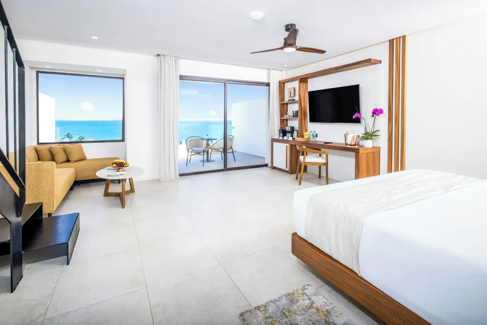 Suite living area with king bed, sofa, desk, TV, and ocean balcony at Majestic Mirage Costa Mujeres.