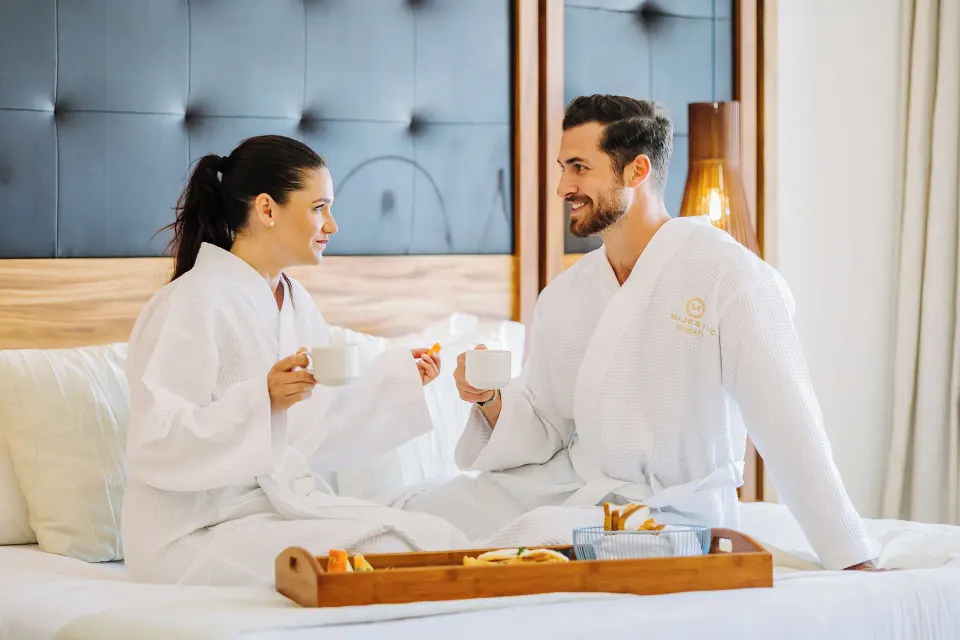 Couple in robes enjoying breakfast in bed at Majestic Mirage Costa Mujeres.