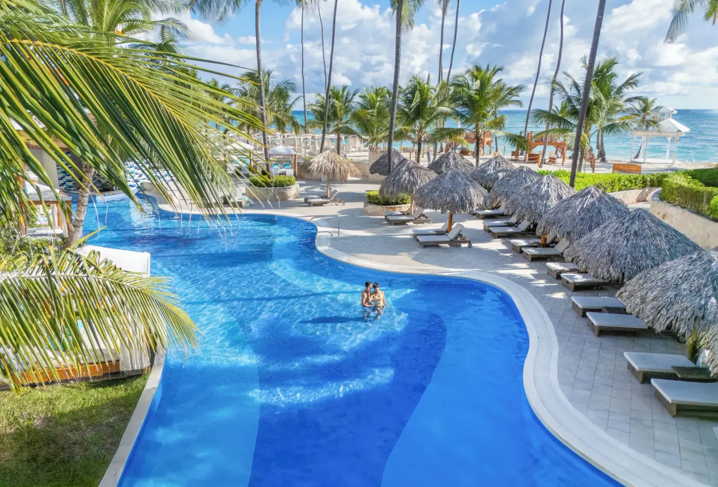 Beachfront pool with palm trees and thatched shade at Majestic Mirage Punta Cana.