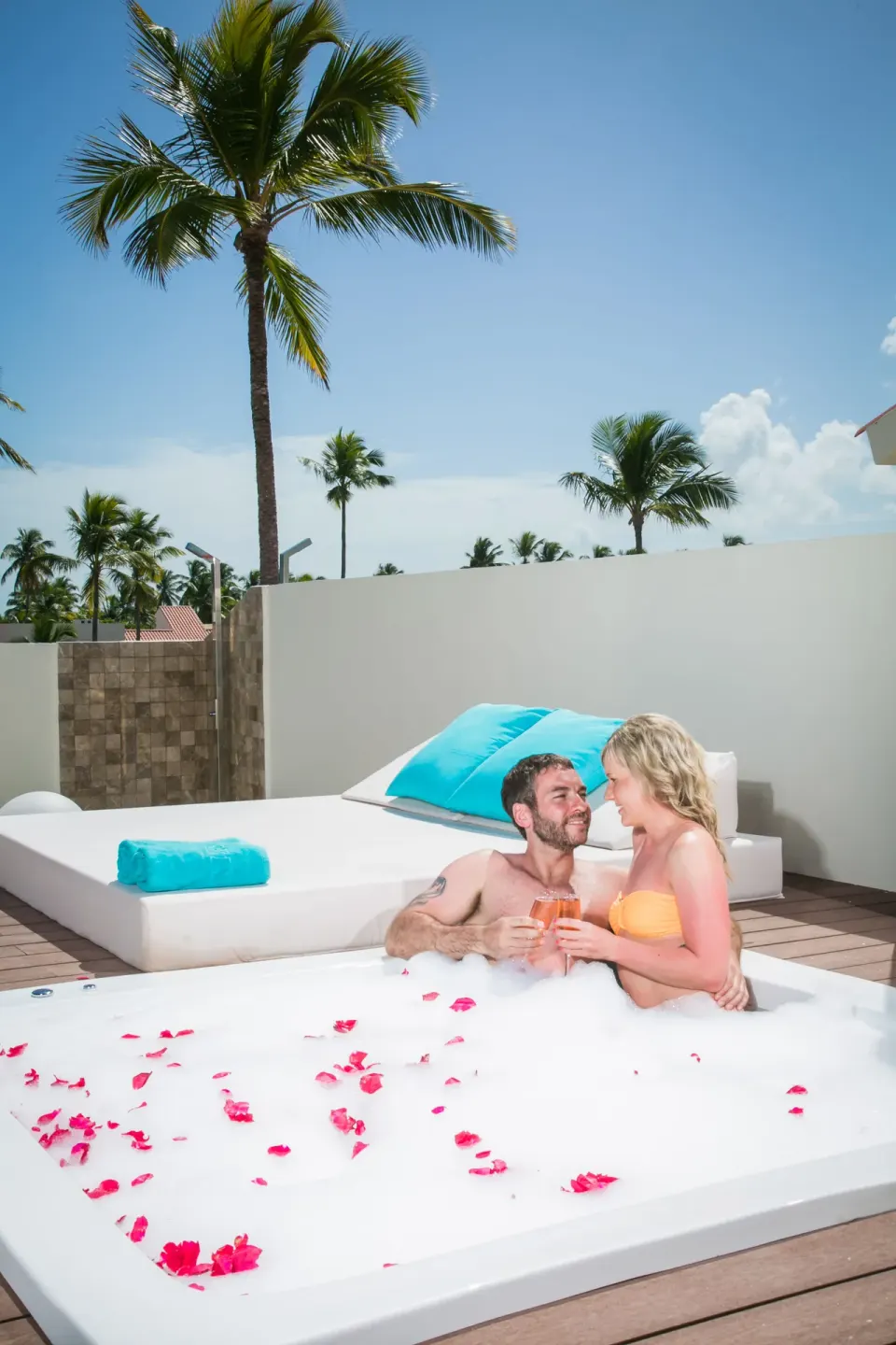 Couple in a rooftop outdoor Jacuzzi at Majestic Mirage Punta Cana with daybed and palms behind.